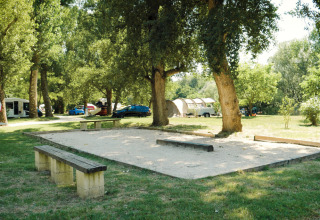 Legeplads og petanquebane i det grønne på Camping La Plage i Occitanie, Frankrig, omgivet af træer.