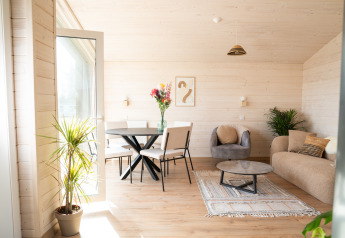 Lyst og moderne opholdsstue i en lodge på Zomerlicht i Nederlandene med planter, sofa og spisebord.
