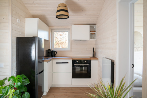 Cucina compatta moderna con frigo nero, macchina da caffè e piante in un lodge a Slowlodge 2, Zomerlicht.