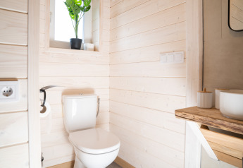 Moderne badeværelse med hvidt toilet, træpaneler, lille vindue og plante, taget på Slowlodge 2, Zomerlicht, Holland.