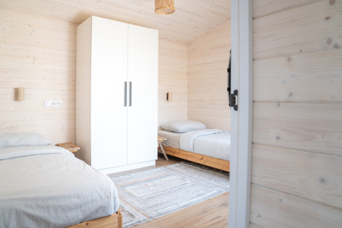 Camera doppia luminosa con due letti singoli, armadio bianco e pareti in legno presso Slowlodge 2 a Zomerlicht.