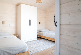 Camera doppia luminosa con due letti singoli, armadio bianco e pareti in legno presso Slowlodge 2 a Zomerlicht.