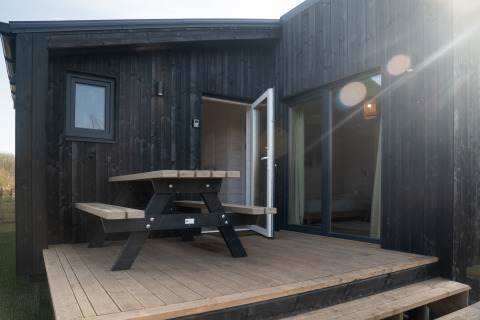 Lodge in legno nero Slowlodge 2 a Zomerlicht, Paesi Bassi, con patio, tavolo da picnic e porta aperta.