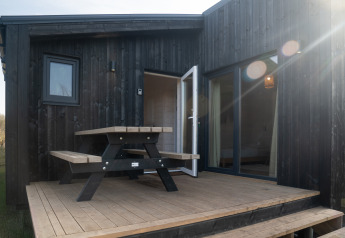 Sort træhytte kaldet Slowlodge 2 ved Zomerlicht i Holland med terrasse, picnicbord og åben dør.