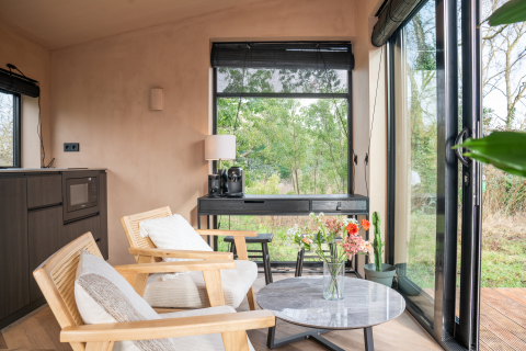 Lichte, moderne lodge-inrichting bij Slowcabin in Zomerlicht, Nederland, met grote ramen en tuinzicht.