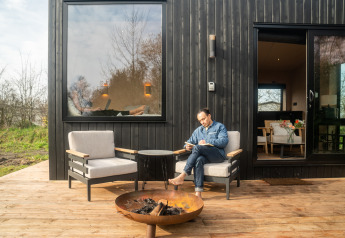 Uomo che legge davanti a una moderna cabina Slowcabin nera con sedie comode e braciere circolare.