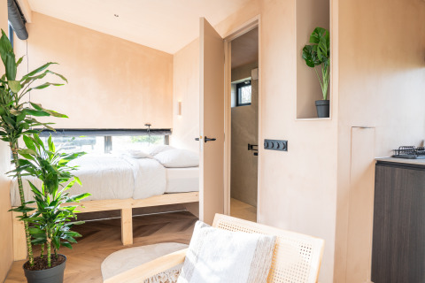 Lichte, minimalistische slaapkamer in Slowcabin bij Zomerlicht, Nederland, met planten en natuurlijk licht.