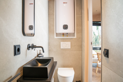 Modern badkamerinterieur in Slowcabin bij Zomerlicht, Nederland, met zwarte wastafel en boiler.
