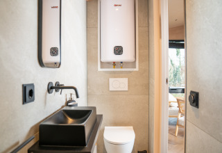 Modern badkamerinterieur in Slowcabin bij Zomerlicht, Nederland, met zwarte wastafel en boiler.