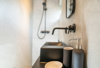 Minimalistische badkamer met zwarte kraan en zeepdispenser in Slowcabin bij Zomerlicht, Nederland.