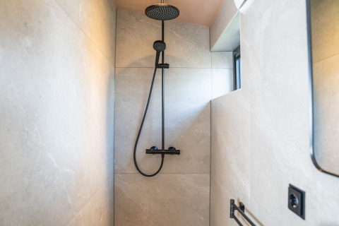 Moderne douche in Slowcabin bij Zomerlicht, Nederland, met een stijlvolle zwarte douchekop en armatuur.