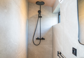 Moderne douche in Slowcabin bij Zomerlicht, Nederland, met een stijlvolle zwarte douchekop en armatuur.