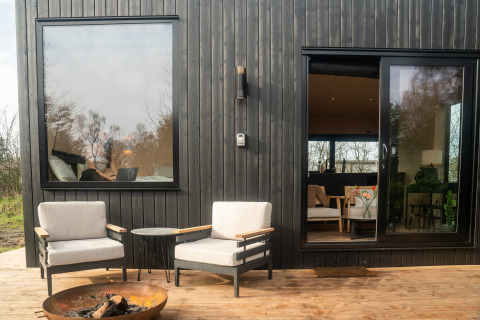 Buitenpatio van Slowcabin te Zomerlicht, Nederland, met twee stoelen, vuurkorf en houten gevel.