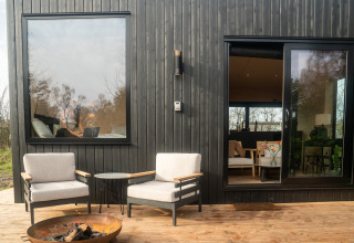 Buitenpatio van Slowcabin te Zomerlicht, Nederland, met twee stoelen, vuurkorf en houten gevel.