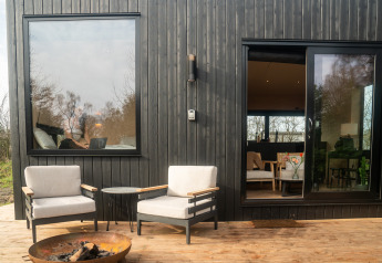 Patio esterno di Slowcabin a Zomerlicht, Paesi Bassi, con due sedie, braciere e pareti in legno scuro.