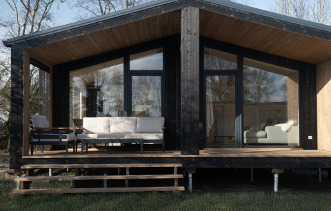 Slowlodge Sage: Zwarte houten lodge met grote ramen, moderne veranda en comfortabele tuinmeubels.