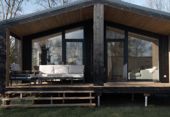 Slowlodge Sage: Zwarte houten lodge met grote ramen, moderne veranda en comfortabele tuinmeubels.