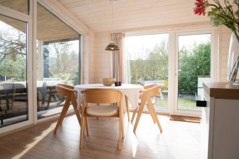 Lichte en moderne eetruimte in Slowlodge Sage bij Zomerlicht, Nederland, met houten meubels en grote ramen.