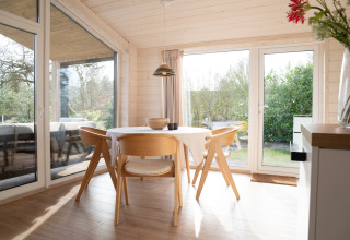 Lichte en moderne eetruimte in Slowlodge Sage bij Zomerlicht, Nederland, met houten meubels en grote ramen.