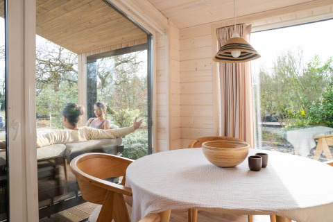 Binnen in Slowlodge Sage bij Zomerlicht in Nederland, met houten tafel en mensen op het terras buiten.
