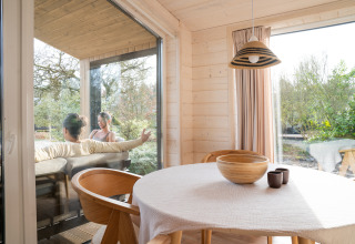 Binnen in Slowlodge Sage bij Zomerlicht in Nederland, met houten tafel en mensen op het terras buiten.