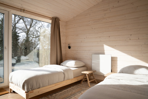 Lichte slaapkamer met houten bekleding, twee eenpersoonsbedden en groot raam bij Slowlodge Sage, Zomerlicht.