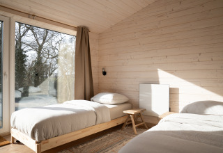 Lichte slaapkamer met houten bekleding, twee eenpersoonsbedden en groot raam bij Slowlodge Sage, Zomerlicht.