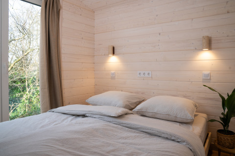 Slaapkamer met lichte houten wanden, tweepersoonsbed, groot raam en sfeerverlichting in Slowlodge Sage.