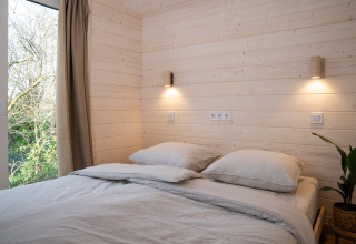 Slaapkamer met lichte houten wanden, tweepersoonsbed, groot raam en sfeerverlichting in Slowlodge Sage.