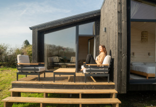 Donna rilassata sulla terrazza di Slowlodge 2, una moderna baita in legno con comodi arredi esterni.