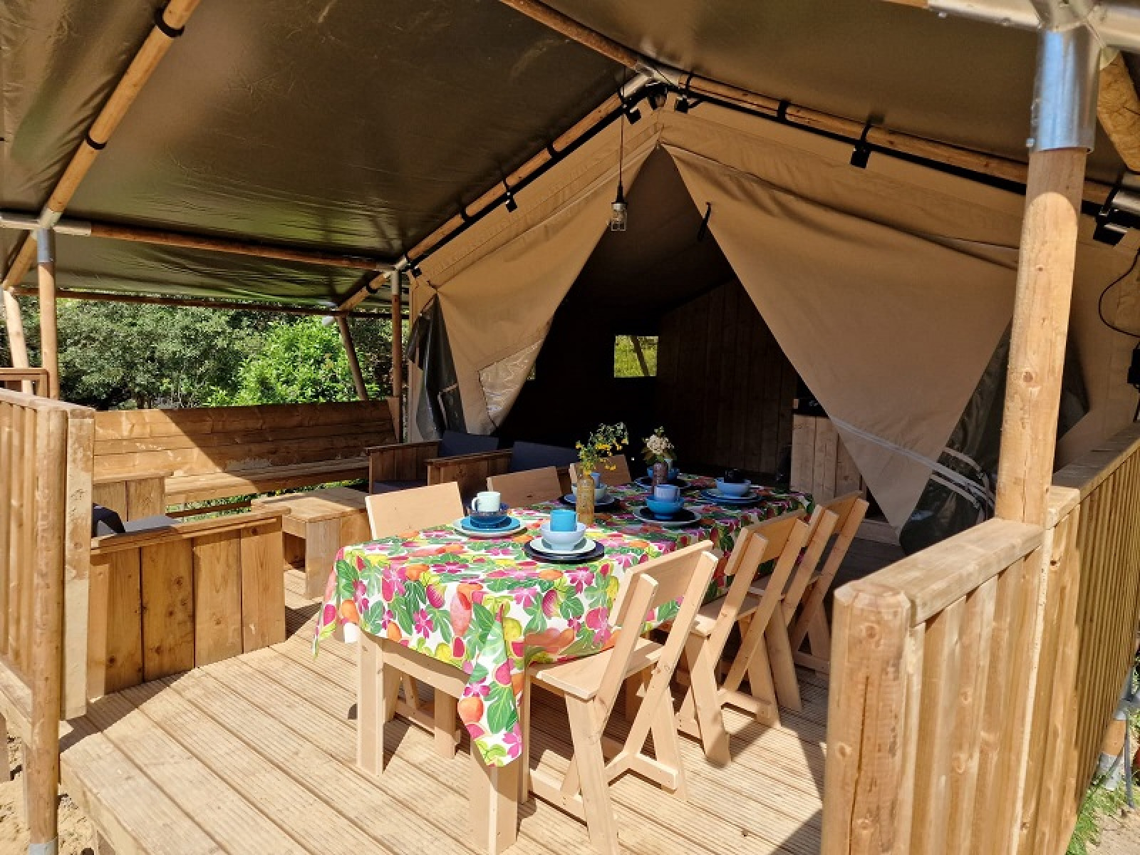Safaritent met overdekt houten terras en kleurrijke eettafel bij Domaine La Sauzette in Frankrijk.