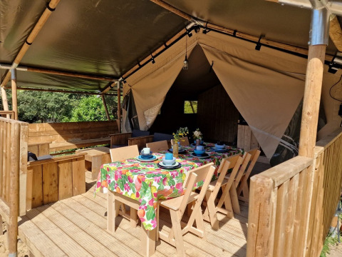 Safari-Zelt mit überdachter Holzterrasse und buntem Esstisch im Domaine La Sauzette, Frankreich.