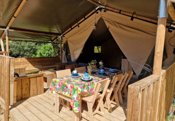 Safaritent met overdekt houten terras en kleurrijke eettafel bij Domaine La Sauzette in Frankrijk.