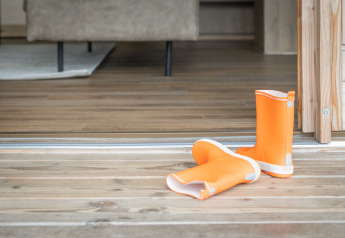 Paire de bottes de pluie orange posée sur la terrasse en bois devant l’entrée d’un hébergement glamping.