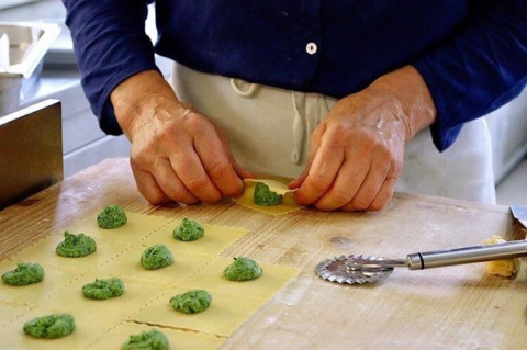 Iemand maakt verse ravioli met groene vulling op een houten werkblad in een Italiaanse keuken in Lombardije.