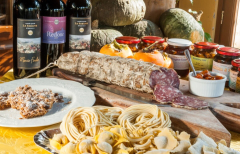 Italienische Spezialitäten wie Wurst, Pasta, Rotwein und Marmelade auf dem Tisch in der Lombardei.