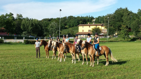 Cinco jinetes a caballo con un instructor en un campo verde en Agriturismo Le Sorgive e Le Volpi, Lombardía, Italia.
