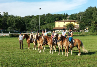 Five riders on horses with an instructor in a green field at Agriturismo Le Sorgive e Le Volpi, Lombardy, Italy.