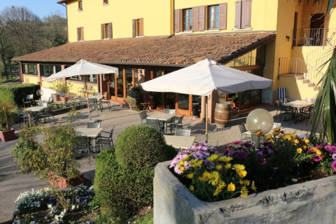 Terrazza esterna con tavoli, ombrelloni e fiori davanti a una casa di campagna gialla in Lombardia, Italia.