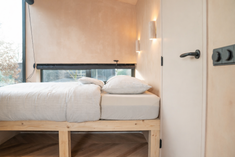 Lichte, minimalistische slaapkamer met houten bedframe en grote ramen in Slowcabin Zomerlicht, Nederland.