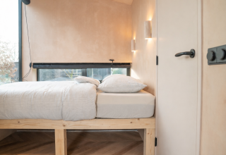 Lichte, minimalistische slaapkamer met houten bedframe en grote ramen in Slowcabin Zomerlicht, Nederland.