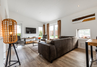 Modern living room with brown sofas, TV, large windows and warm lighting at Schaelsbergerbosch Garden House.