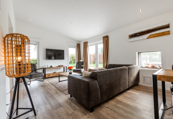 Salon moderne avec canapé brun, grande fenêtre et décoration chaleureuse au Schaelsbergerbosch Garden House.