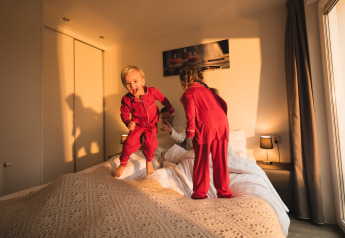 Deux enfants en pyjama rouge sautent joyeusement sur un lit au Resort Mooi Bemelen, Pays-Bas, au soleil.