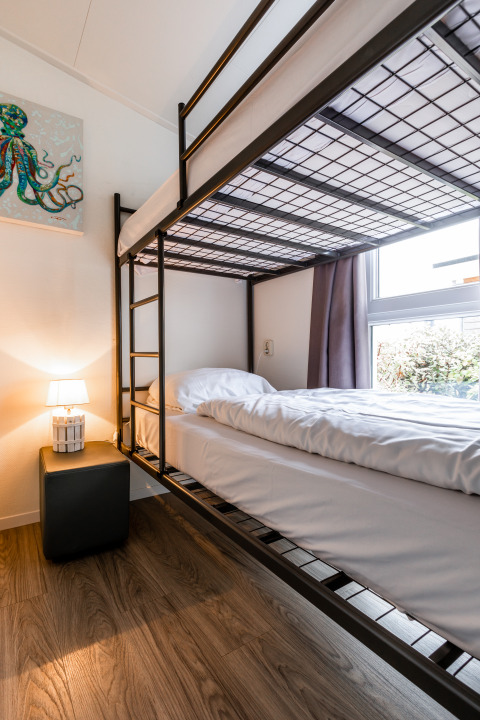 Moderne stapelbed in een gezellige kamer met houtenvloer, nachtkastje, lamp en raam in Resort Mooi Bemelen.