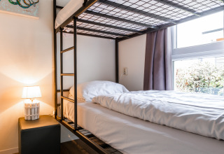 Moderne stapelbed in een gezellige kamer met houtenvloer, nachtkastje, lamp en raam in Resort Mooi Bemelen.