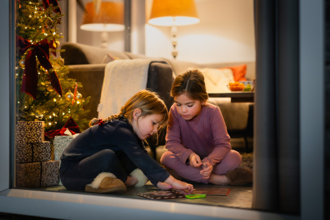 Twee kinderen spelen bij een kerstboom en cadeautjes in een gezellig vakantiehuisje op Resort Mooi Bemelen.