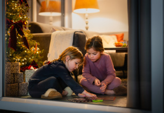 Twee kinderen spelen bij een kerstboom en cadeautjes in een gezellig vakantiehuisje op Resort Mooi Bemelen.