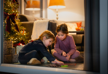 Two children play on the floor near a decorated Christmas tree and presents in a cozy lodge at Resort Mooi Bemelen.