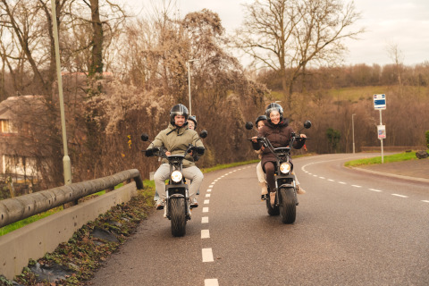 Twee koppels op scooters rijden langs een bochtige weg bij Resort Mooi Bemelen in Nederland.